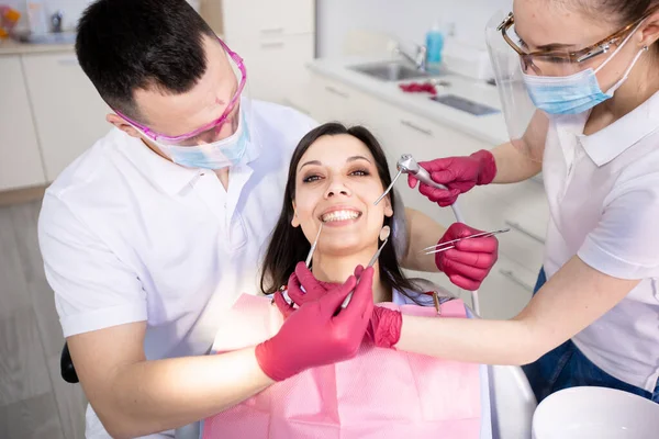 Smiling young woman in a dental chair. Two dentists check the patients teeth. Preventive trip to the dentist. Dentistry, healthcare, medicine — Stock Photo, Image