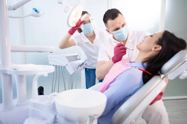 Dos dentistas tratan los dientes de un paciente joven. Mujer sentada en una silla dental. Salud, medicina — Foto de Stock