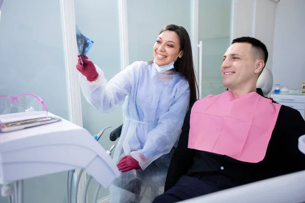 Happy female dentist and patient examining x-ray of healthy teeth. Caries prevention, teeth cleaning. A young man visits the dentist — Stok fotoğraf