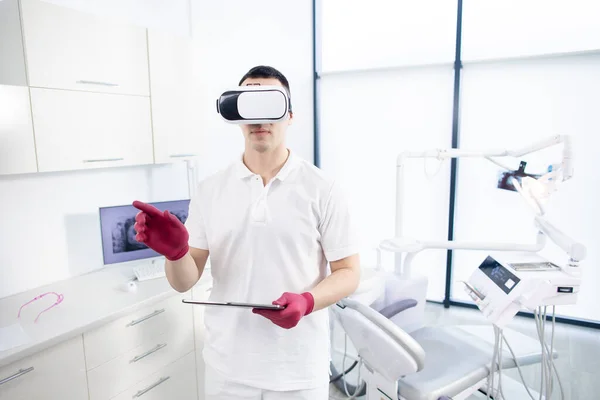 A male dentist in uniform stands in the office and checks the digital image before the patients visit. The latest technologies in dentistry, 3D images, virtual reality — Foto de Stock