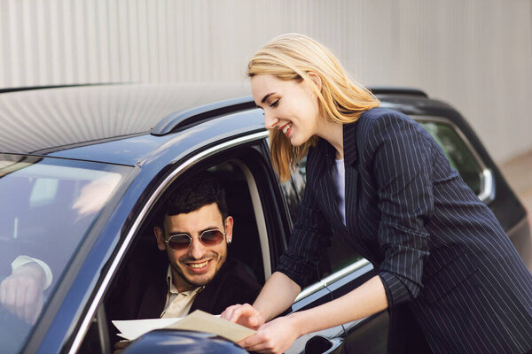 A young man rents a car. Employee of the dealer center shows documents near the car Stock Picture