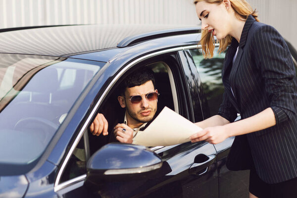 A young man rents a car. Employee of the dealer center shows documents near the car Royalty Free Stock Images