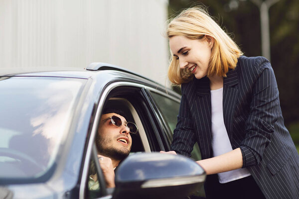 Business people talking near car park. The man in the glasses is sitting in the car, the woman stands next to him Stock Photo