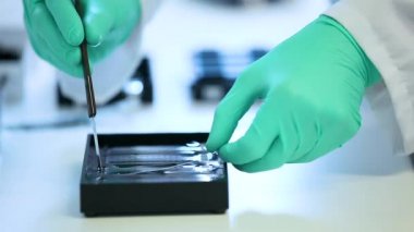 Yeşil eldivenli bilimadamı bir makinedeki tüpler ile test ve araştırma yapıyor. Sadece beyaz bir laboratuvarda bulunan mikrobiyologların ellerini görebiliyoruz. Yakın çekim görüntüsü. Bilim deneyi konsepti