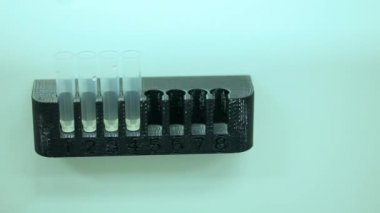 Yeşil eldivenli bir bilim adamı laboratuardaki numune tüpleriyle test ve araştırma yapıyor. Sadece beyaz bir laboratuvarda bulunan mikrobiyologların ellerini görebiliyoruz. Yakın çekim görüntüsü. Bilim deneyi konsepti