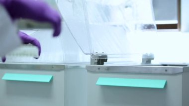 Mor eldivenli bilim adamı bir makinedeki tüpler ile test ve araştırma yapıyor. Sadece beyaz bir laboratuvarda bulunan mikrobiyologların ellerini görebiliyoruz. Yakın çekim görüntüsü. Bilim deneyi konsepti