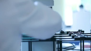 Mor eldivenli bilim adamı bir makinedeki tüpler ile test ve araştırma yapıyor. Beyaz bir laboratuvarda, yakın plan bilim deneyi konseptinde olan sadece mikrobiyologların ellerini görebiliyoruz.