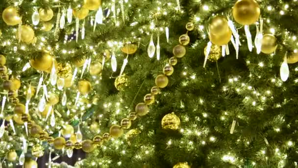 Uma vista de um ramo de uma árvore de Natal decorada com bolas douradas e guirlandas luminosas que está na rua. — Vídeo de Stock