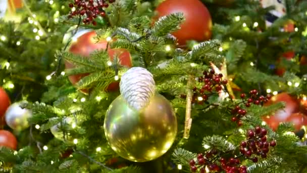 A view of a Christmas tree covered with snow and decorated with a fir cone, gold and red balls and glowing garlands. — Stock Video