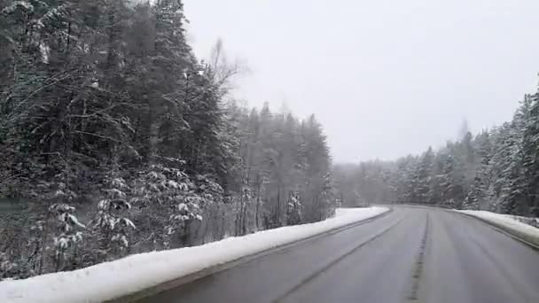 Utsikten genom vindrutan på en bil i rörelse på vägen i en snötäckt vinterskog som går in i en skarp sväng. — Stockvideo