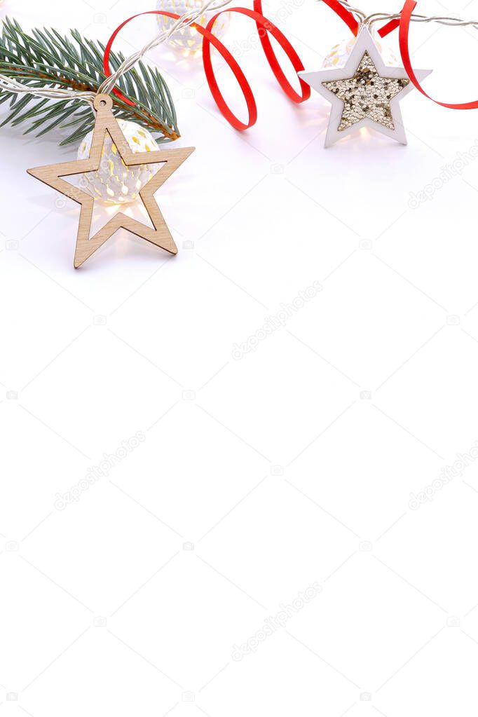 Christmas composition of fir branches, wooden stars, garlands of white luminous balls and red ribbon on a white background