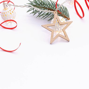 Noel kompozisyonu köknar dalları, tahta yıldızlar, beyaz toplardan oluşan çelenkler ve beyaz arka planda kırmızı kurdele.