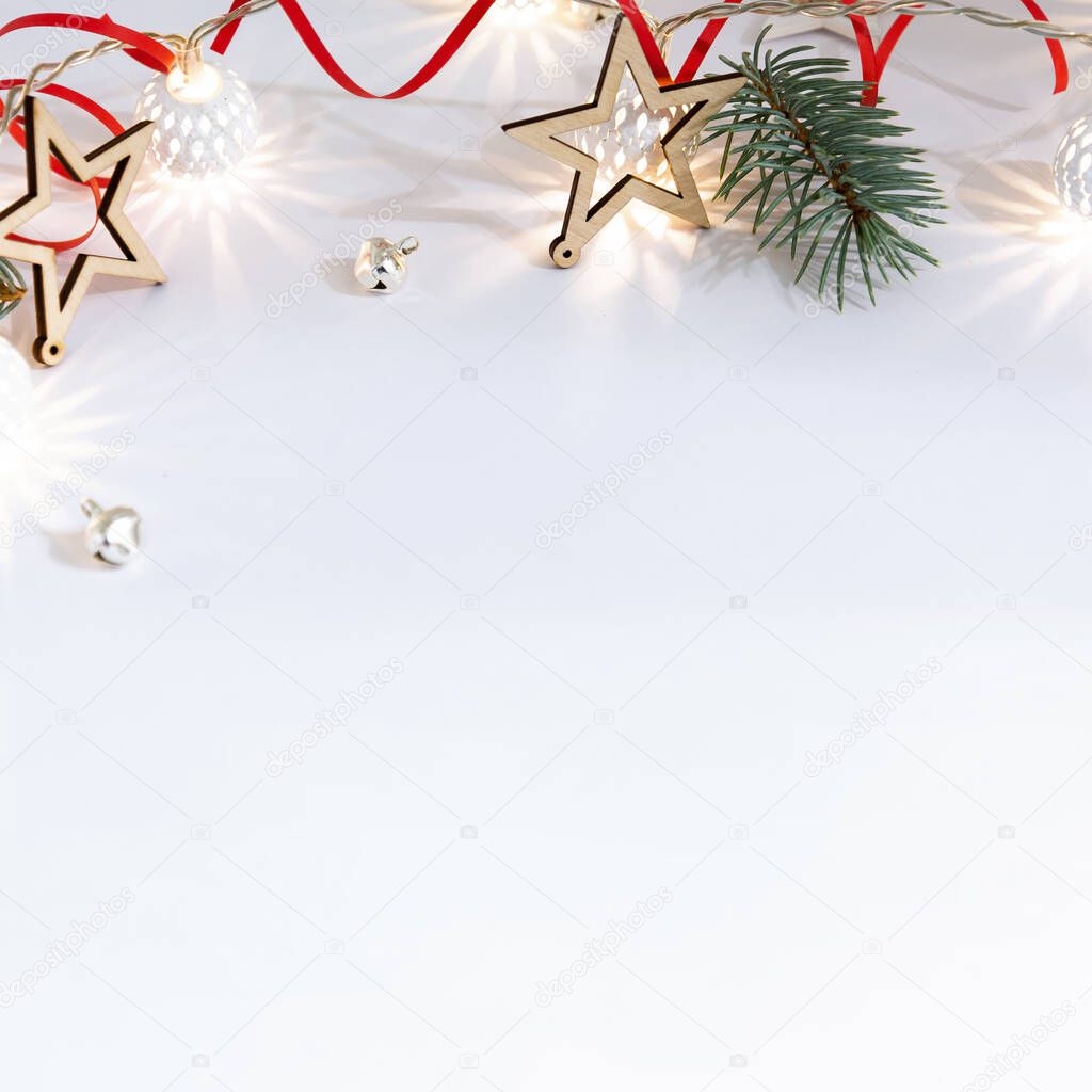 Christmas composition of wooden stars, a garland of white luminous balls, fir branches, bells and a red ribbon on a white background