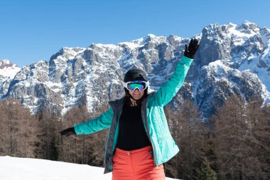 Kayak yaptıktan sonra renkli bir kayak takımı, kask ve güneş gözlüğü takan bir kadın dağ zirvelerinin arka planında duruyor. Spor konsepti, insanlar, seyahat
