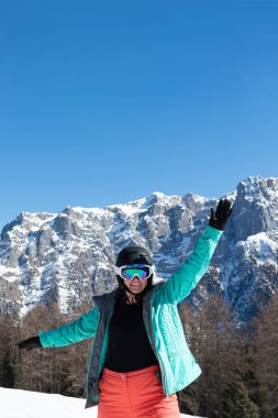Kayak yaptıktan sonra renkli bir kayak takımı, kask ve güneş gözlüğü takan bir kadın dağ zirvelerinin arka planında duruyor. Spor konsepti, insanlar, seyahat