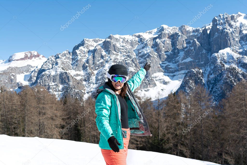 A woman in a colorful ski suit, helmet and sunglasses after skiing stands against the backdrop of mountain peaks. Sports concept, people, travel