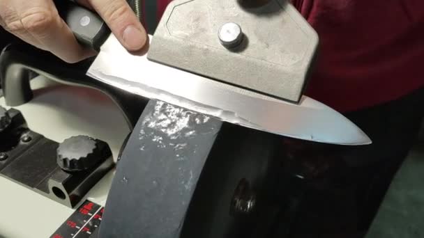 Un homme aiguise un couteau de chef sur un broyeur à eau électrique sur une pierre grise grossière. — Video