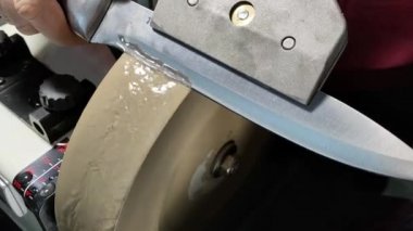 Bir adam şefin bıçağını ince taneli bir taşın üzerinde elektrikli su öğütücüsünde biler..