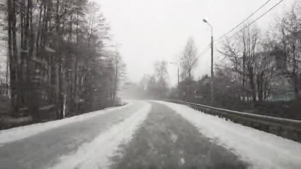 Uitzicht door de voorruit op de snelweg in de winter waarlangs de auto rijdt in zware sneeuw en wind in Rusland. — Stockvideo