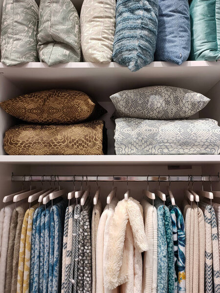 View of a wardrobe with woolen blankets hanging on hangers and pillows and blankets on the shelves