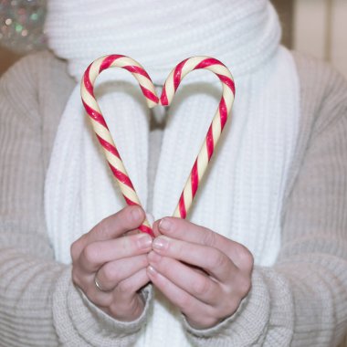 Bej kazak ve beyaz eşarplı yetişkin bir kadın Noel şekerlerini kalp şeklinde tutuyor..
