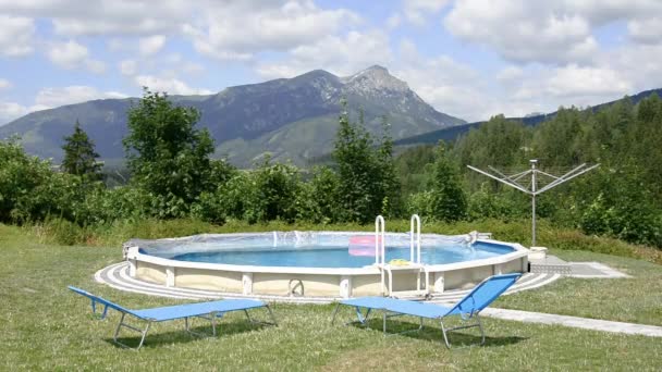 View of the round pool with a pink inflatable ring on the street and sun loungers against the backdrop of mountains. — Stock Video