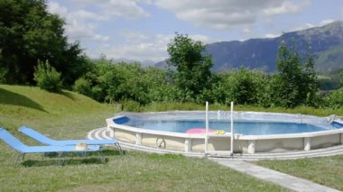 Sokakta pembe şişirilebilir bir yüzükle yuvarlak havuz manzarası ve dağların arka planında güneşlenmeler..