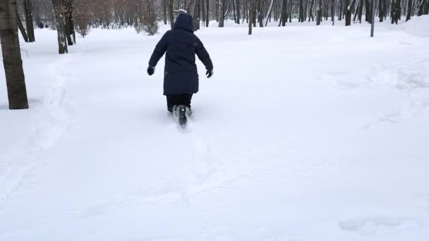 一位身穿蓝色夹克的年轻女子穿过公园里巨大的雪堆. — 图库视频影像