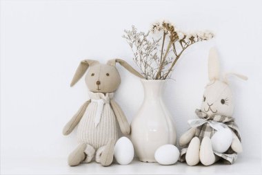 Paskalya kompozisyonu, tavşanların yumuşak oyuncakları ve odanın rafındaki beyaz yumurtalar.