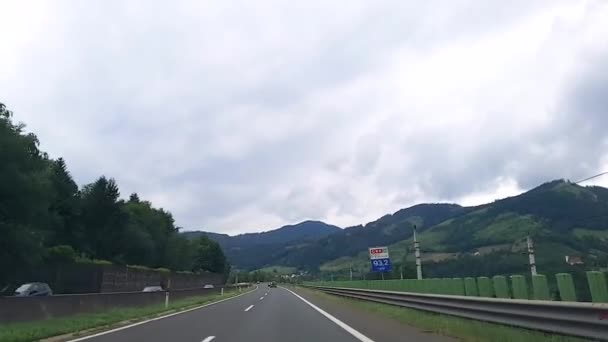 Autriche. Vue à travers le pare-brise de la voiture vers les montagnes, les prairies alpines et l'autoroute par temps nuageux. — Video