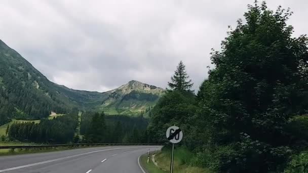 Kilátás a szélvédőn keresztül az autó a hegyekbe, alpesi rétek és az út felhős időben. — Stock videók