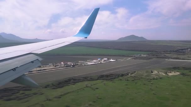 Вид крыла летающего самолета в солнечную погоду над полями, горами и поселениями. — стоковое видео