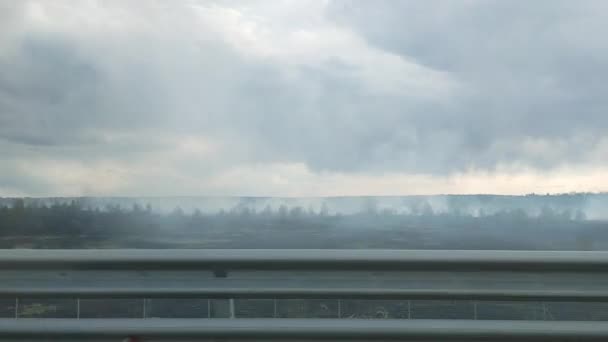 Das Auto fährt auf der Autobahn und durch die Seitenscheibe sieht man ein Feuer auf einem brennenden Feld und Rauch. — Stockvideo