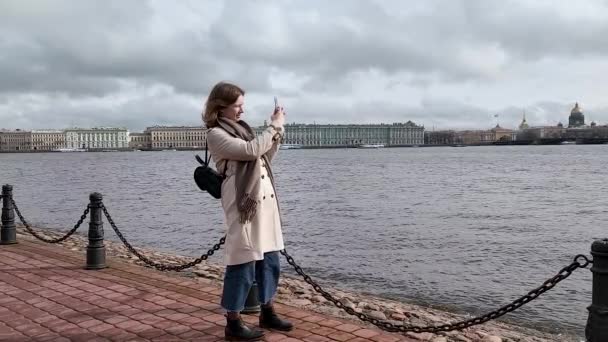 Eine junge Frau mit einem Handy in der Hand fotografiert das Ufer der Newa in St. Petersburg, den Palastplatz und die Isaak-Kathedrale. — Stockvideo