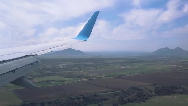 Widok skrzydła latającego samolotu w słoneczną pogodę nad polami, górami i osadami. — Wideo stockowe