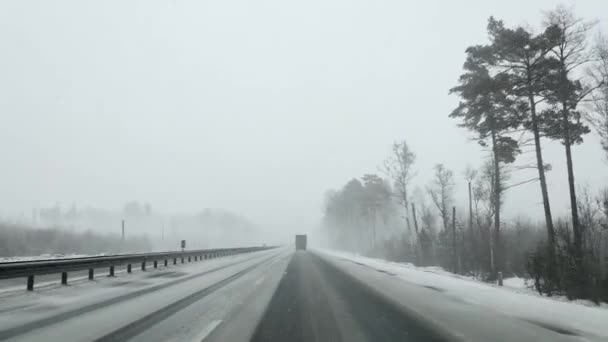 Widok przez przednią szybę samochodu na autostradzie w zimie w obfitych opadów śniegu i ciężarówki. — Wideo stockowe