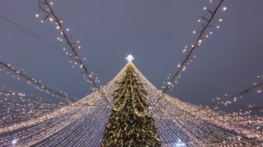 Kırmızı ve altın topları olan bir Noel ağacı manzarası ve gece gökyüzünün arka planında parlayan bir çelenk..