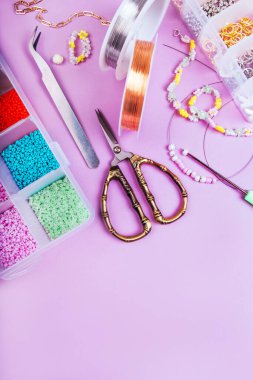 Mücevher, tel, makas ve kolye yapımında kullanılan farklı tohum ve inci boncuklardan oluşan yaratıcı düz tabaka pembe arka planda izole edilmiş..