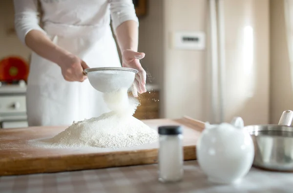 Jonge vrouw zeven meel in de kom in de keuken — Stockfoto