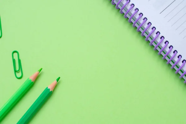 Green pencils, green paper clips and a notebook over a bright green background, with some copy space