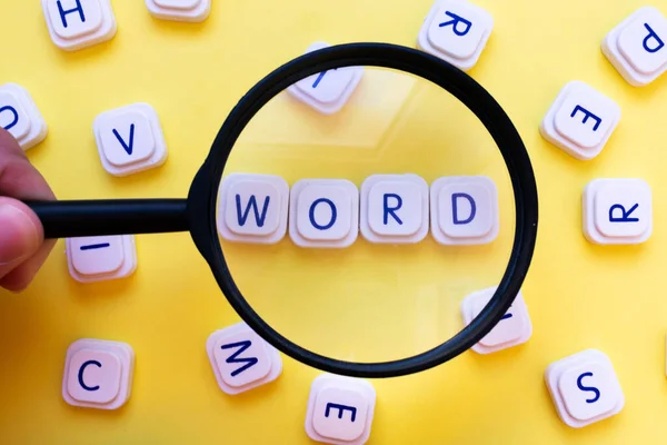 Word made with board game letters, focused by a magnifying glass, surrounded by random letters, over a bright yellow background