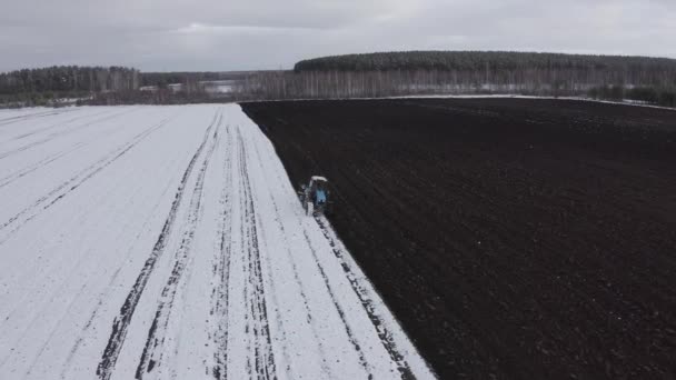 Синий трактор вспахивает поле, покрытое снегом. За трактором чернозем. Россия, Урал. 4K — стоковое видео