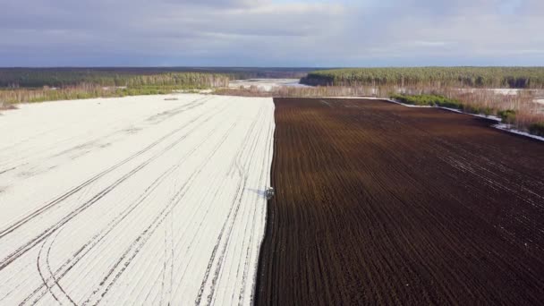 Un tractor azul arada un campo cubierto de nieve. Detrás del tractor hay tierra negra. Rusia, Ural. 4K — Vídeo de stock