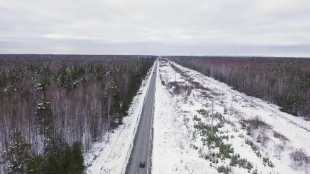 Een blauwe auto rijdt langs een winterasfaltweg. De weg loopt langs de hoogspanningsleidingen. Sneeuw op bomen en wegen. 4K — Stockvideo