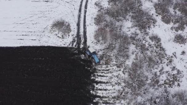 Un tractor azul arada un campo cubierto de nieve. Detrás del tractor hay tierra negra. El borde del campo. Rusia, Ural. 4K — Vídeo de stock
