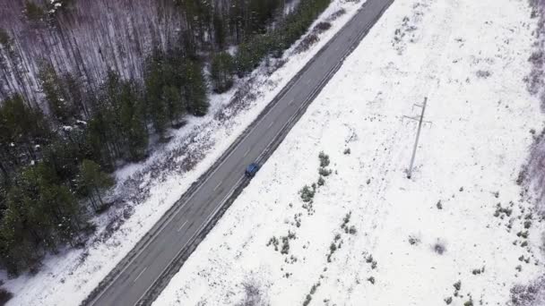 Голубая машина едет по зимней асфальтовой дороге. Дорога проходит по линиям электропередач. Снег на деревьях и обочинах дорог. 4K — стоковое видео