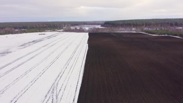 Dolly zoom. Ein blauer Traktor pflügt ein schneebedecktes Feld um. Hinter dem Traktor liegt schwarze Erde. Russland, Ural — Stockvideo