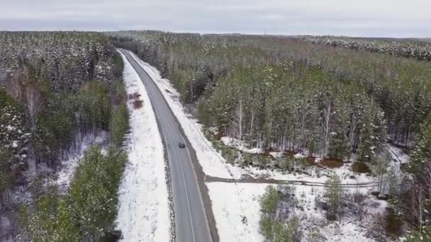 Um carro azul anda ao longo de uma estrada de asfalto de inverno na floresta. Neve nas árvores e nas estradas. 4K — Vídeo de Stock