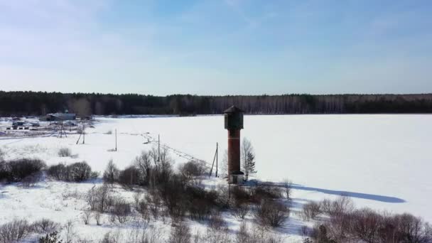 Vliegen in de winter. Oude watertoren op een besneeuwd veld. 4K — Stockvideo