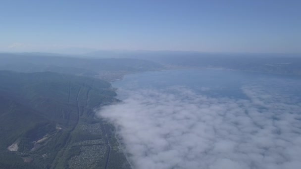 Voando acima das nuvens. Costa do Lago Baikal. Montanhas cobertas de floresta. A Rússia. 4K — Vídeo de Stock
